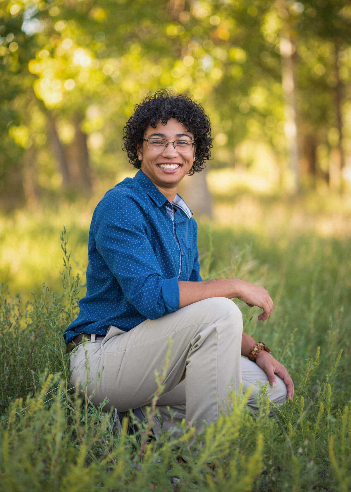 a young man kneeling in a grassy forest area