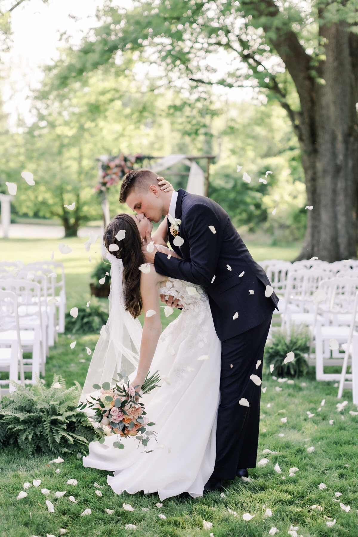 A couple shares a first kiss during the petal toss at their fine art inspired outdoor wedding
