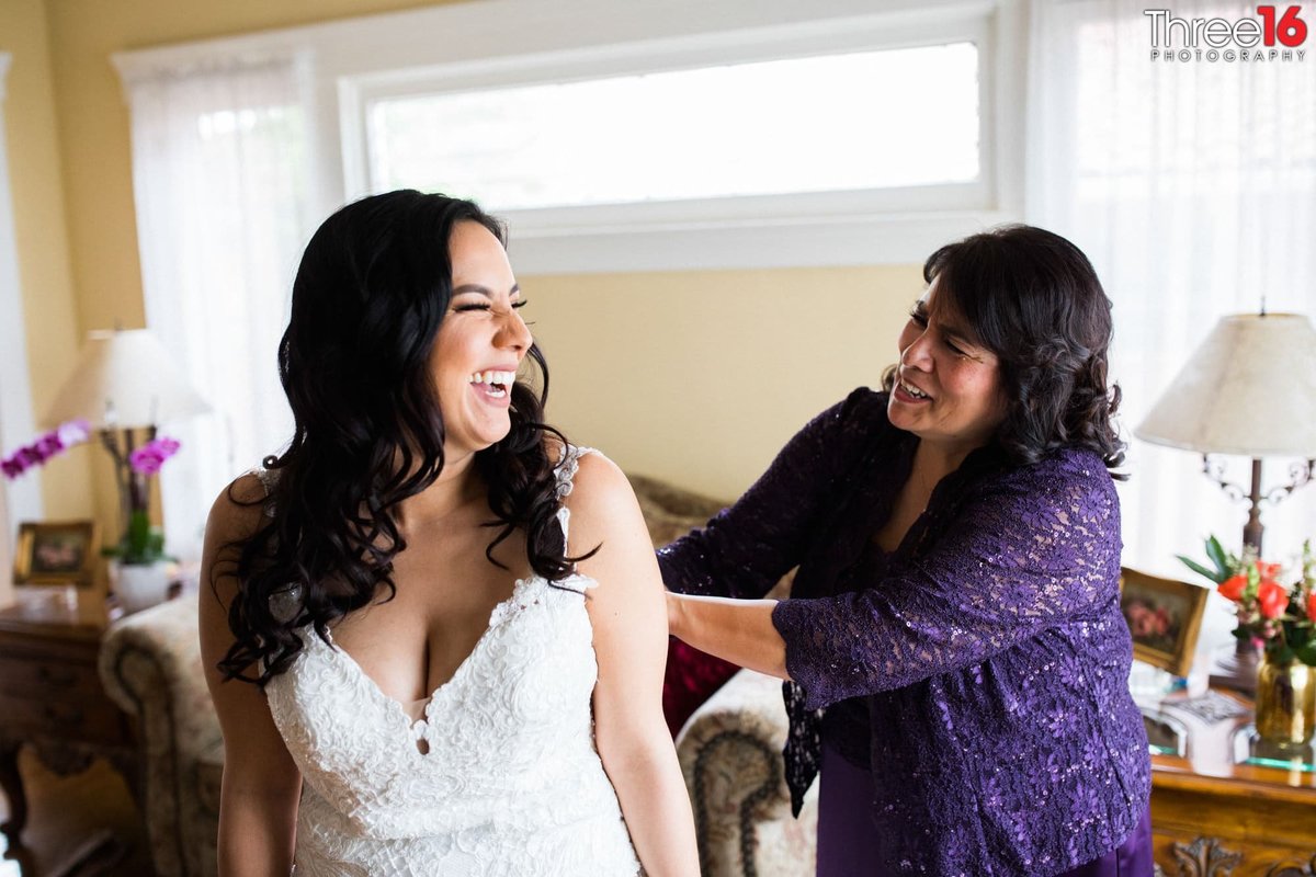 Mother of the Bride helps her daughter button her wedding gown