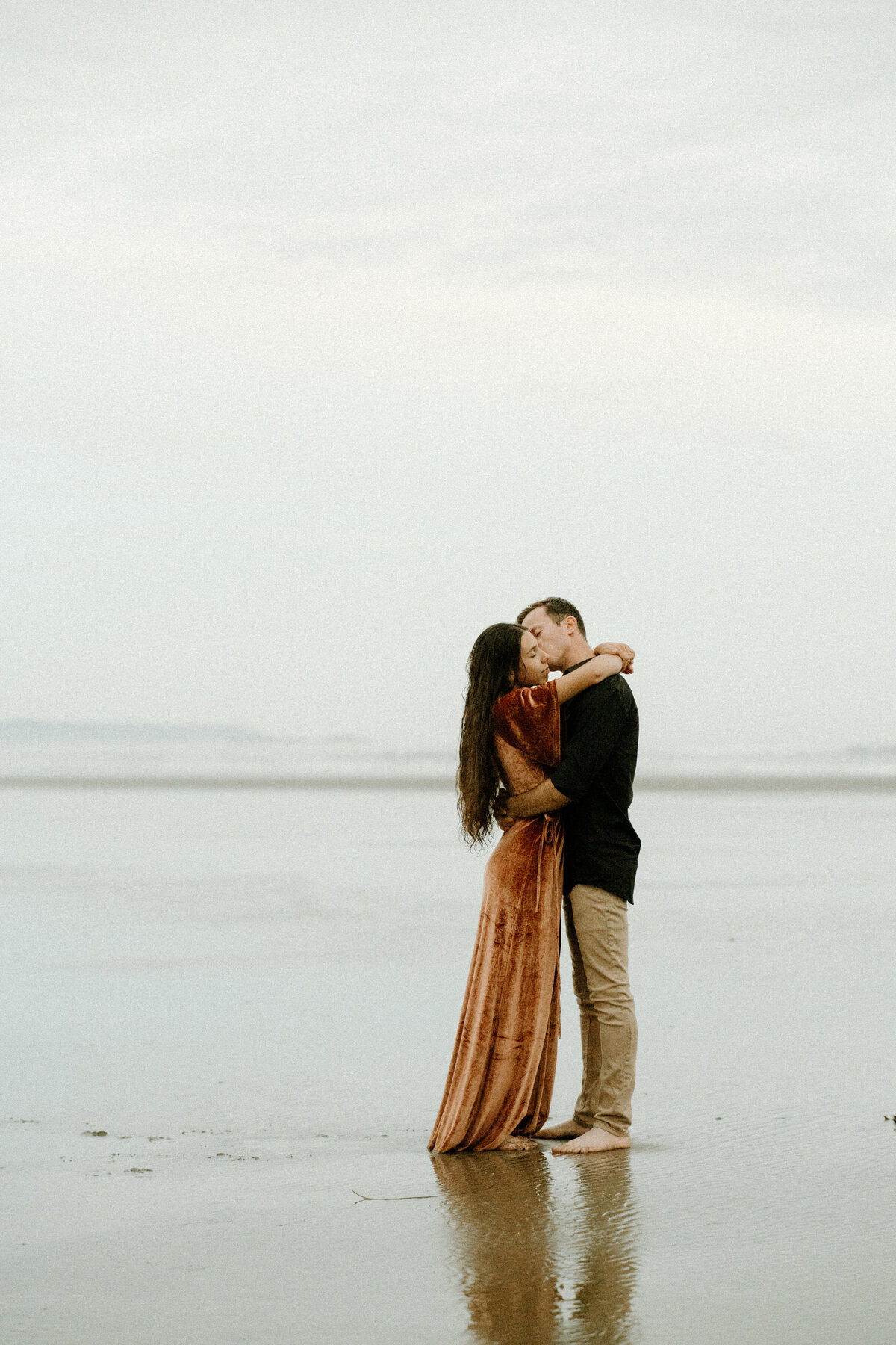 engagement photo of a guy whispering something into a girls ear at the beach