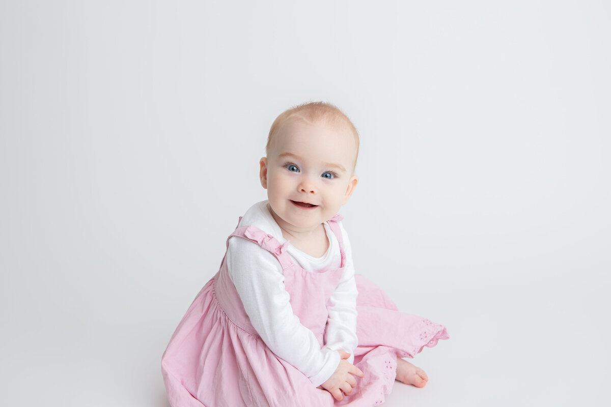 Baby girl in pink sitting  on pure white savage seamless paper backdrop
