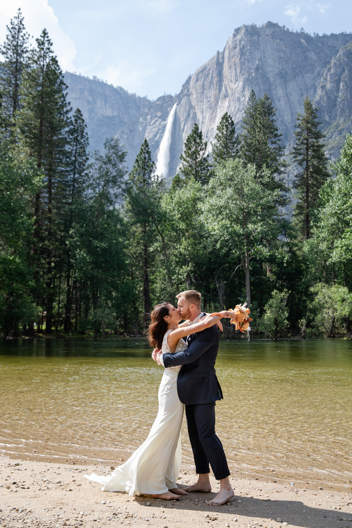 A bride and groom kiss next to the Merced River in Yosemite, California.