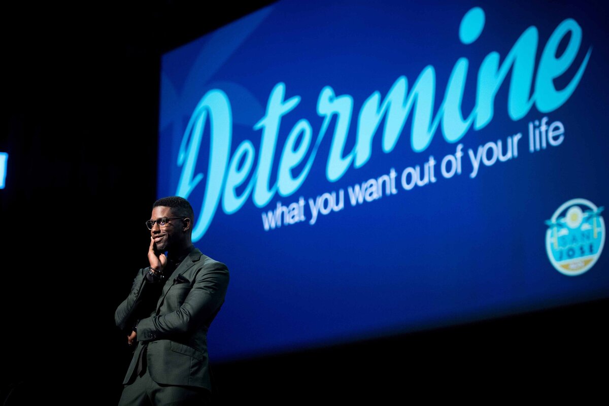 A nicely dressed speaker looks curiously at audience with "Determine what you want out of life" in background