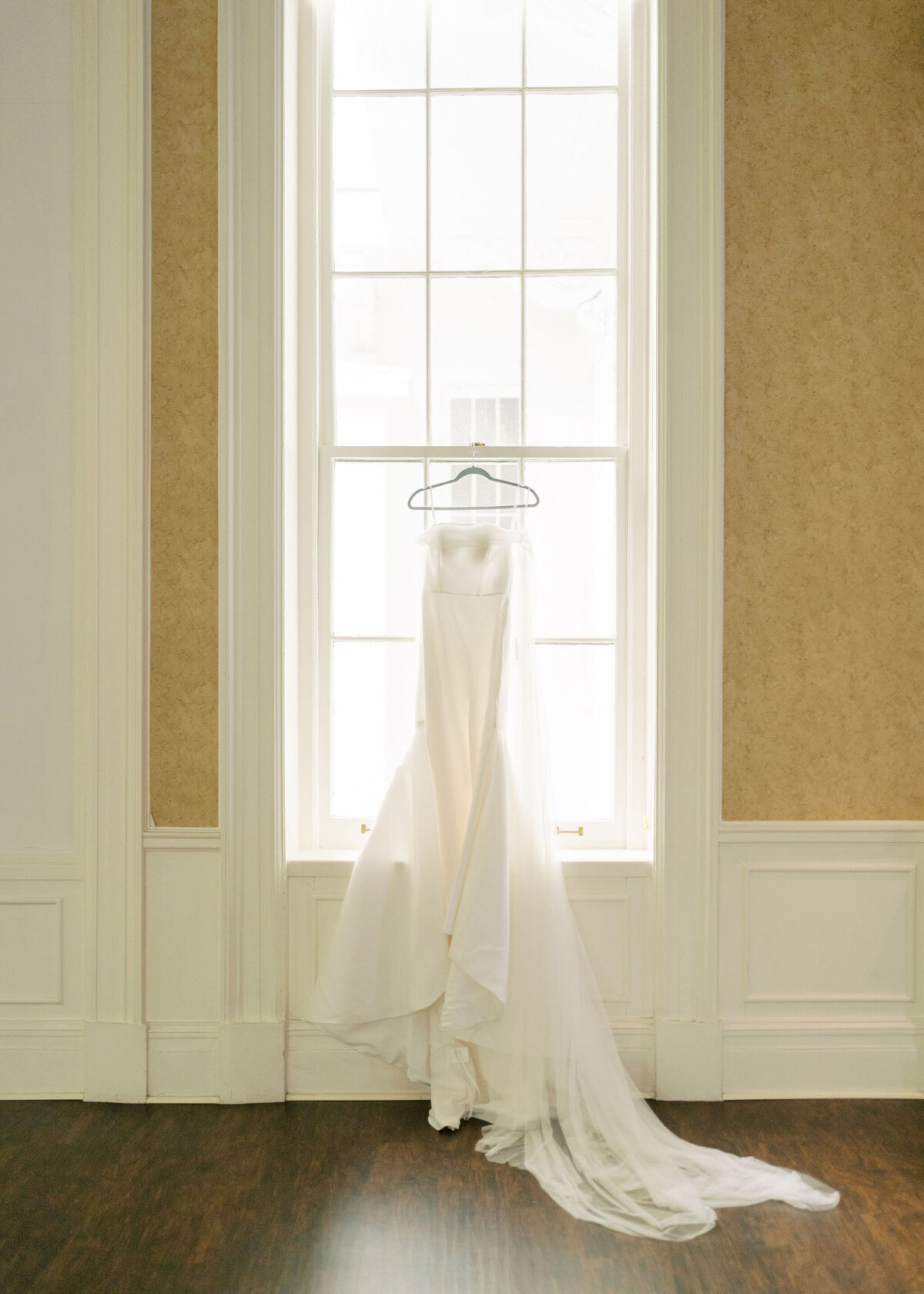 a wedding dress hanging up by a window