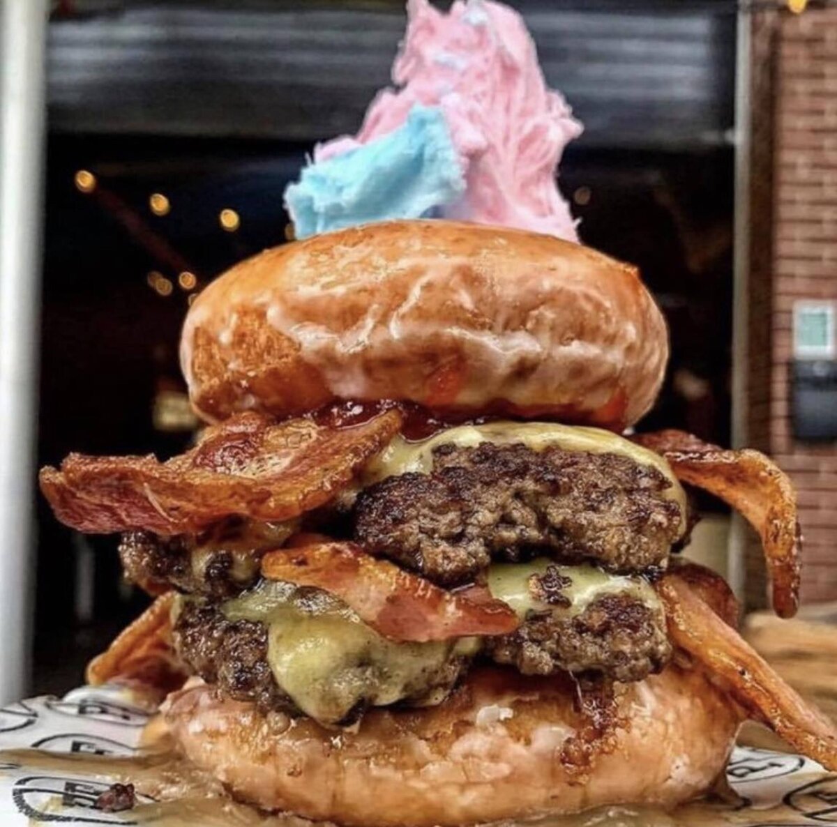 A beef burger with donut bun, bacon , cheese and double patty filling with candy floss on top