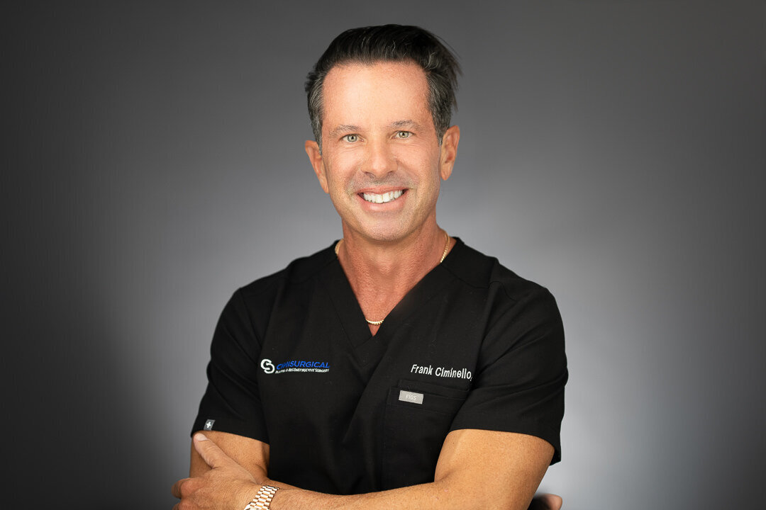 Professional headshot of smiling male doctor in black medical scrubs against gray background, NJ healthcare branding portrait by Alex Kaplan Photo.