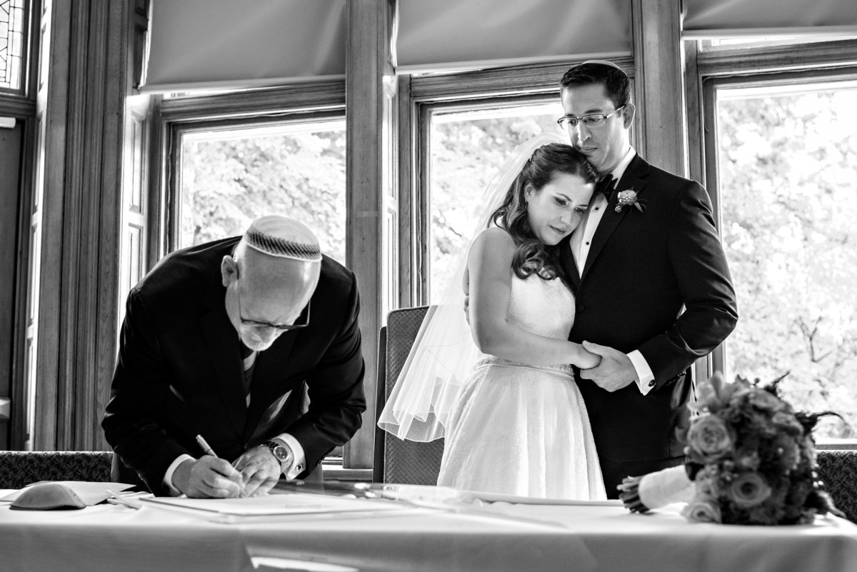 A jewish wedding couple watch as their rabbi signs the ketubah before the ceremony at Temple Beth Hillel.