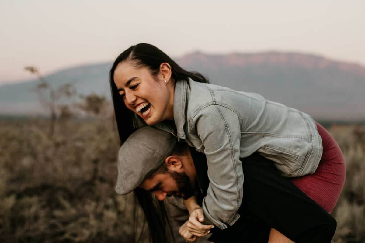woman laughing while on fiancé's back