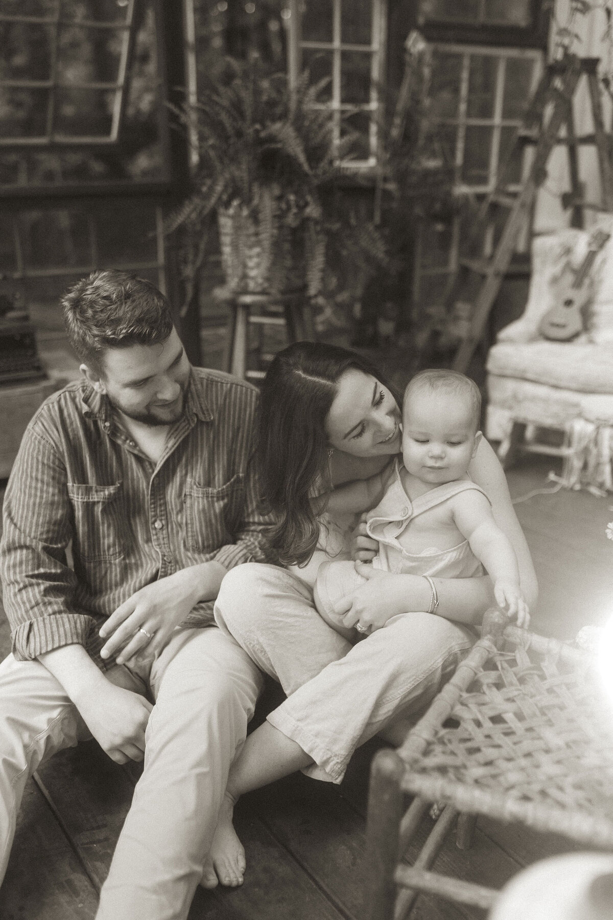 A mother and father kiss on and smile at their baby boy while sitting on the ground at Das Hinterhaus. 
