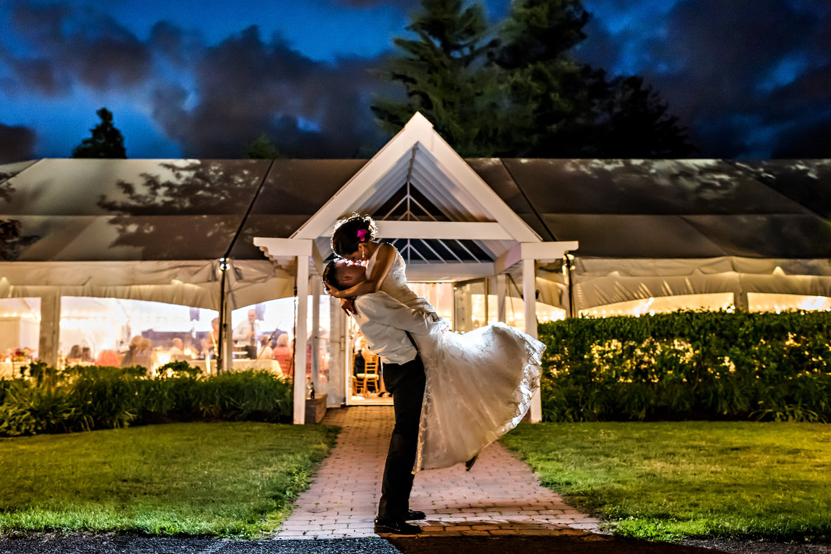 A groom lifts his bride up in the air in front of their reception tent at Pearl S Buck Estate in bucks county.