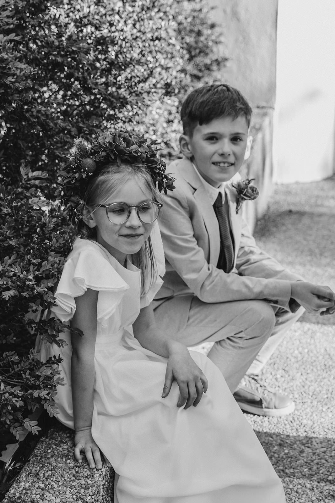 Two small kids in formal outfits sitting down and smiling 