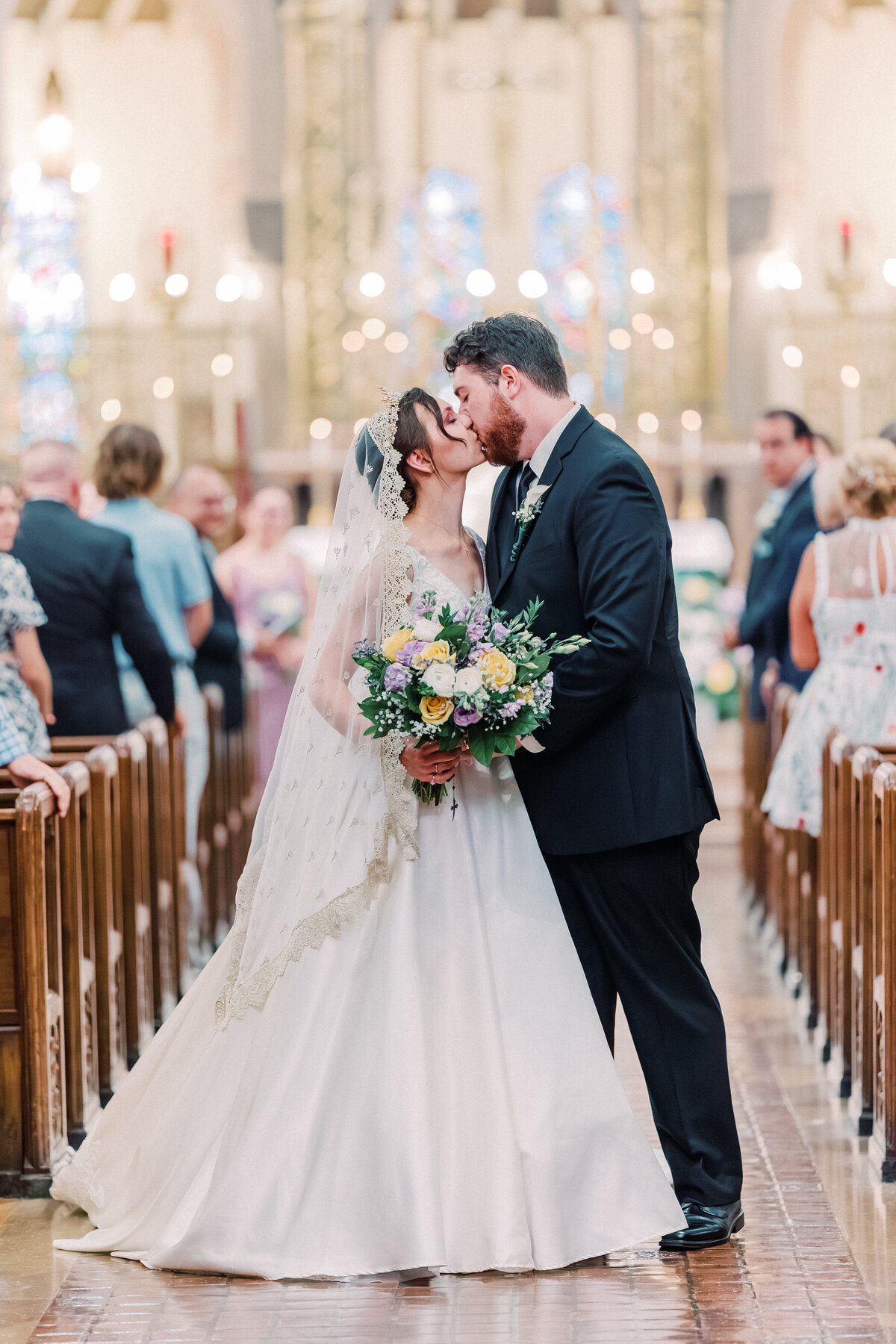 Bride and groom kissing in middle of aisle while guests clap at St Monica St George wedding in Cincinnati