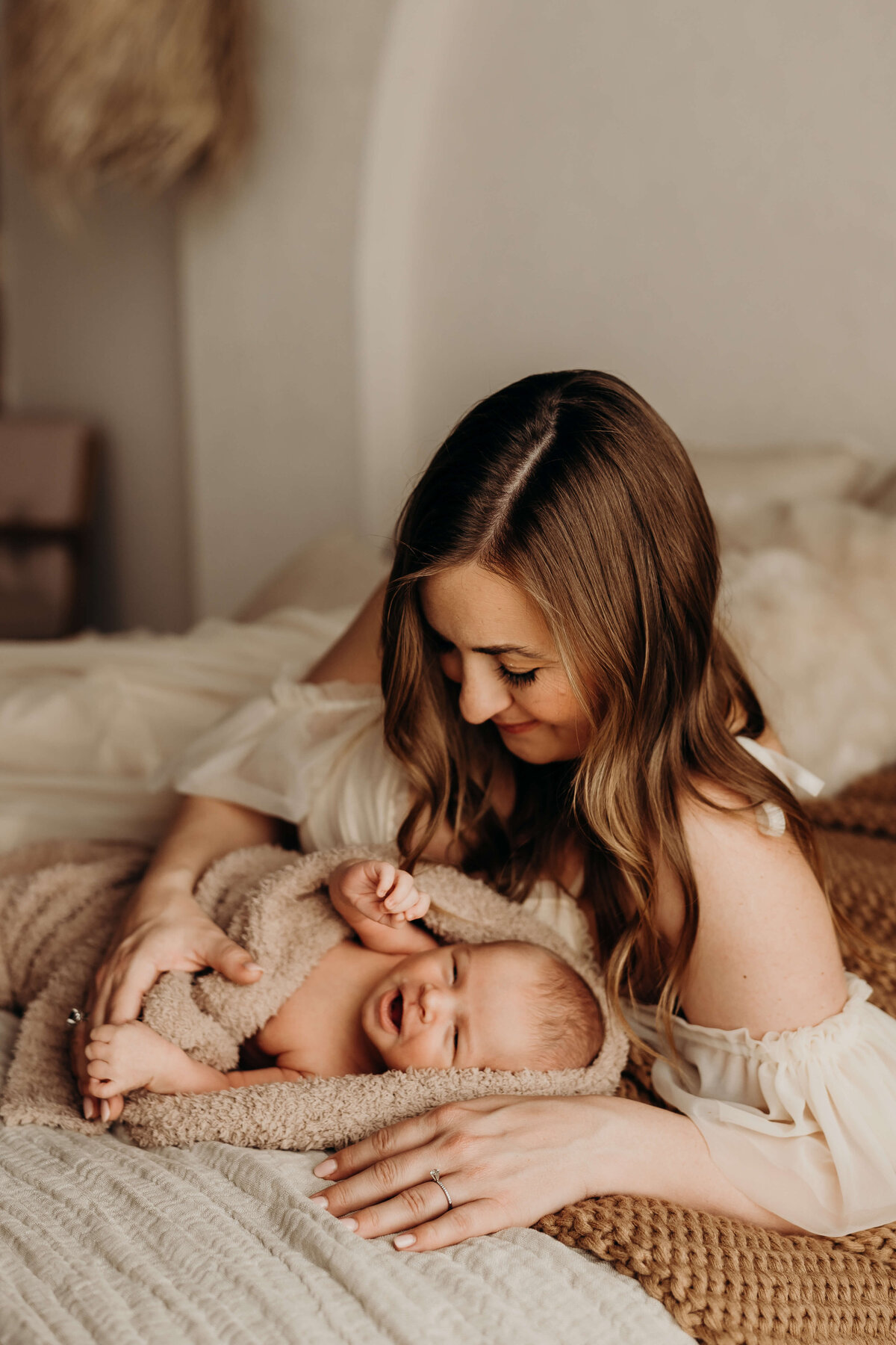 baby smiles as he looks at his mom while laying on a bed