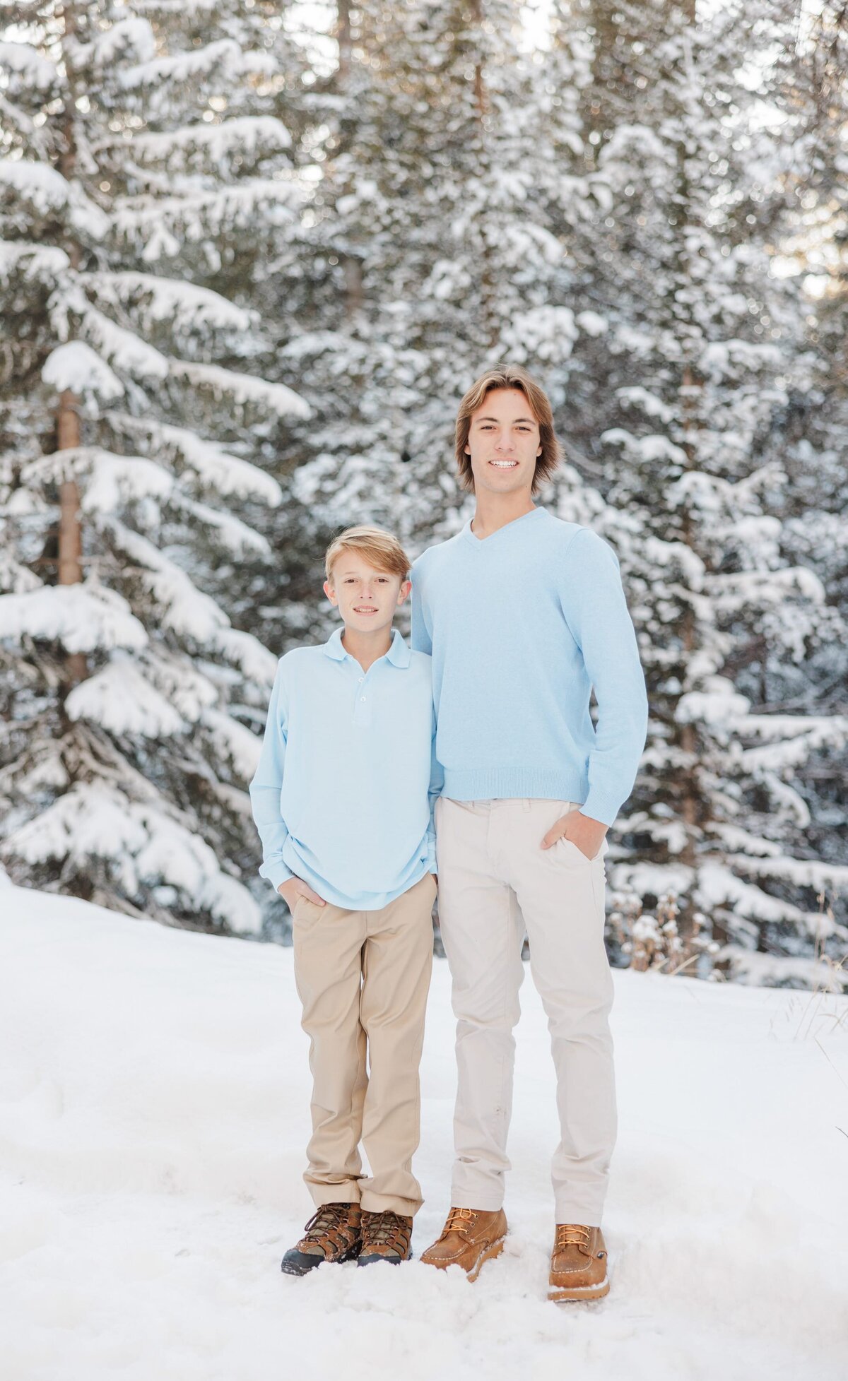 Teen brothers in blue shirts stand with arms around each other smiling in snow