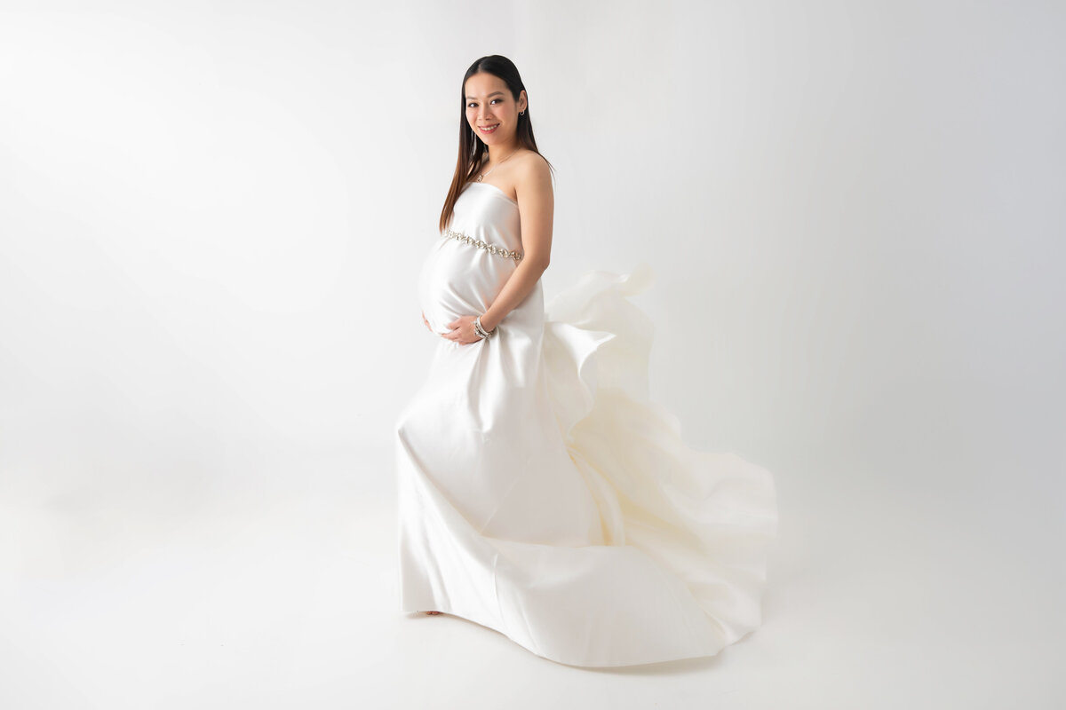 Pregnant woman is draped in a silky white fabric with a rhinestone belt accentuating her pregnant belly. 