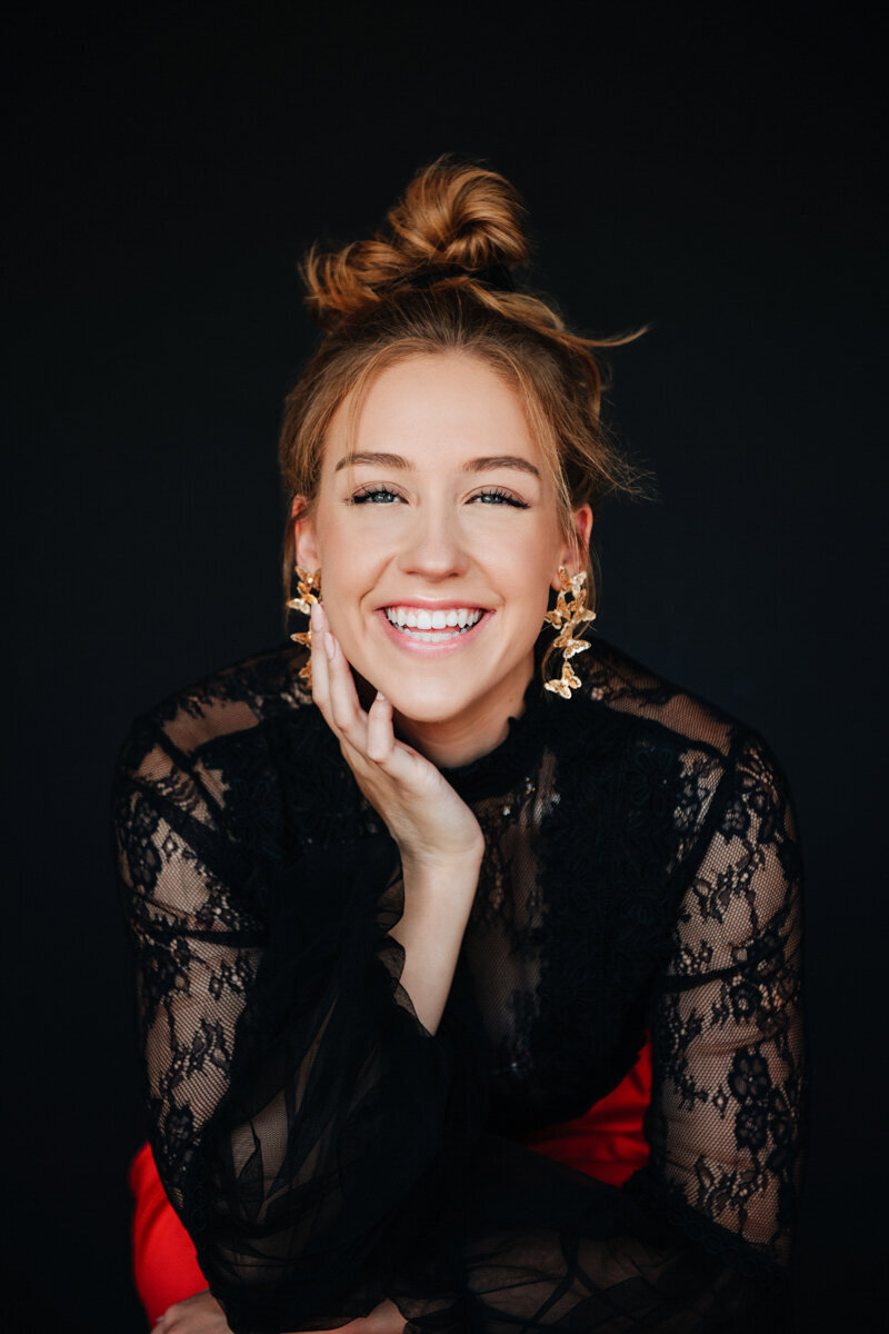 Glamorous studio portrait of a senior girl in black lace, glowing with a joyful smile.