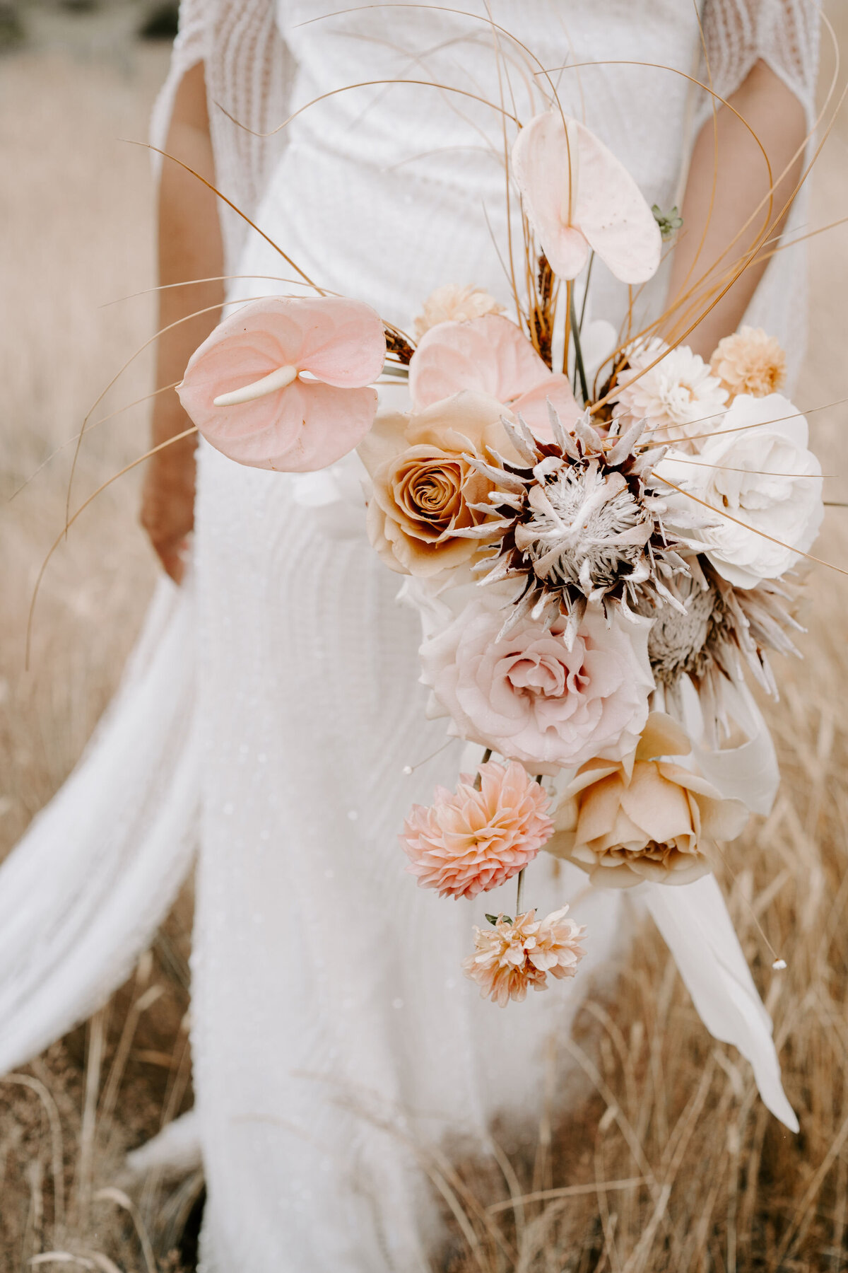 bride walks through field in New Zealand holding lightly coloured pale bouquet