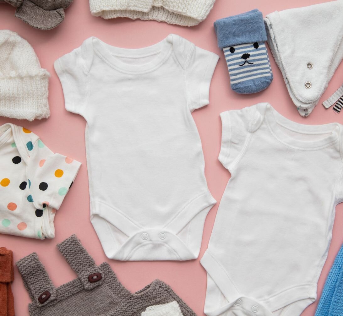 A collection of baby clothes laid out on a pink background.
