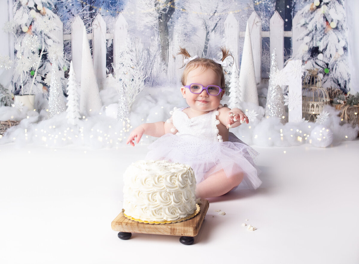 Baby girl sitting infront of cake during first birthday cake smash photoshoot in Franklin Tennessee Photography studio