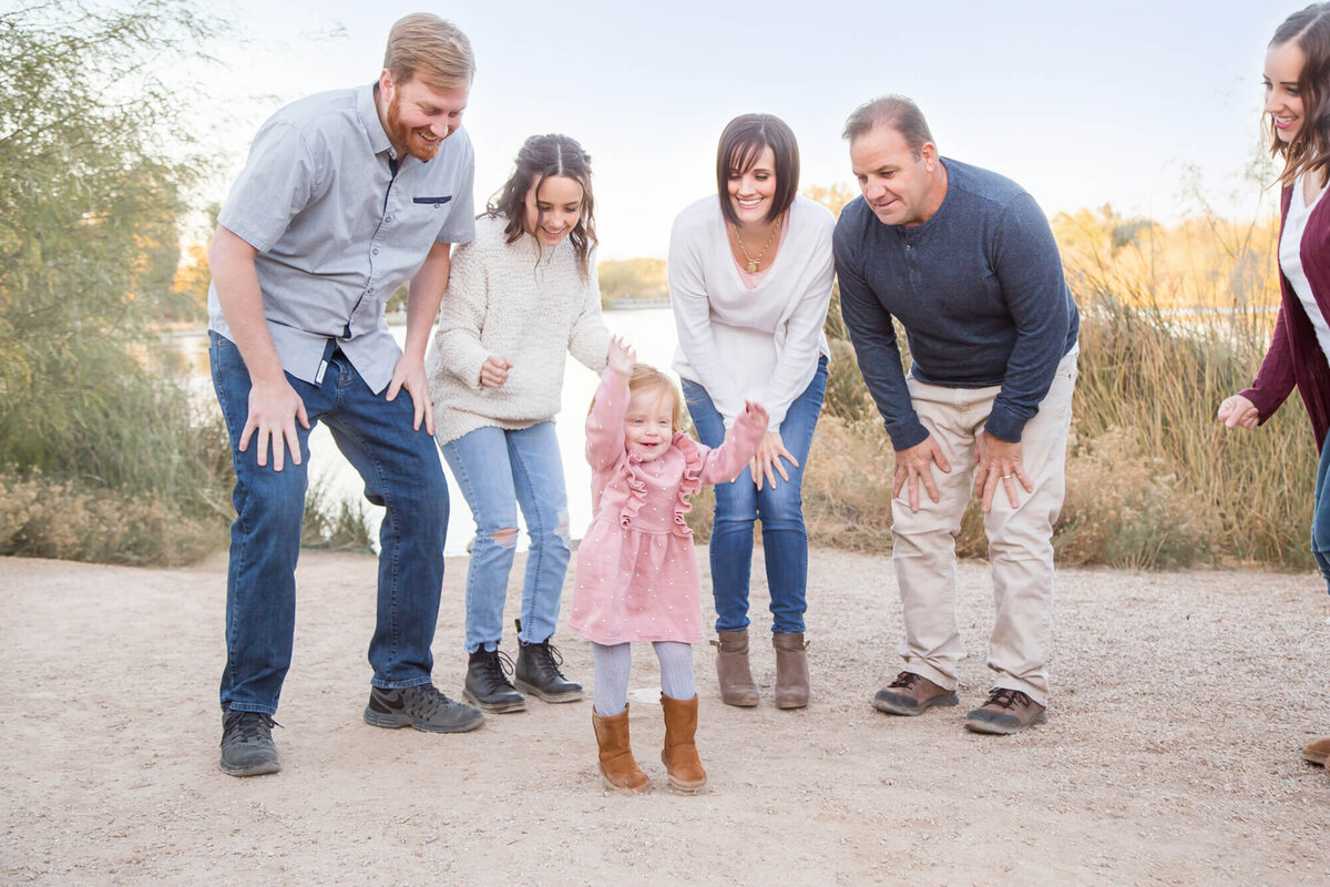 Redheaded toddler girl dancing in crowd of adult family members by desert pond