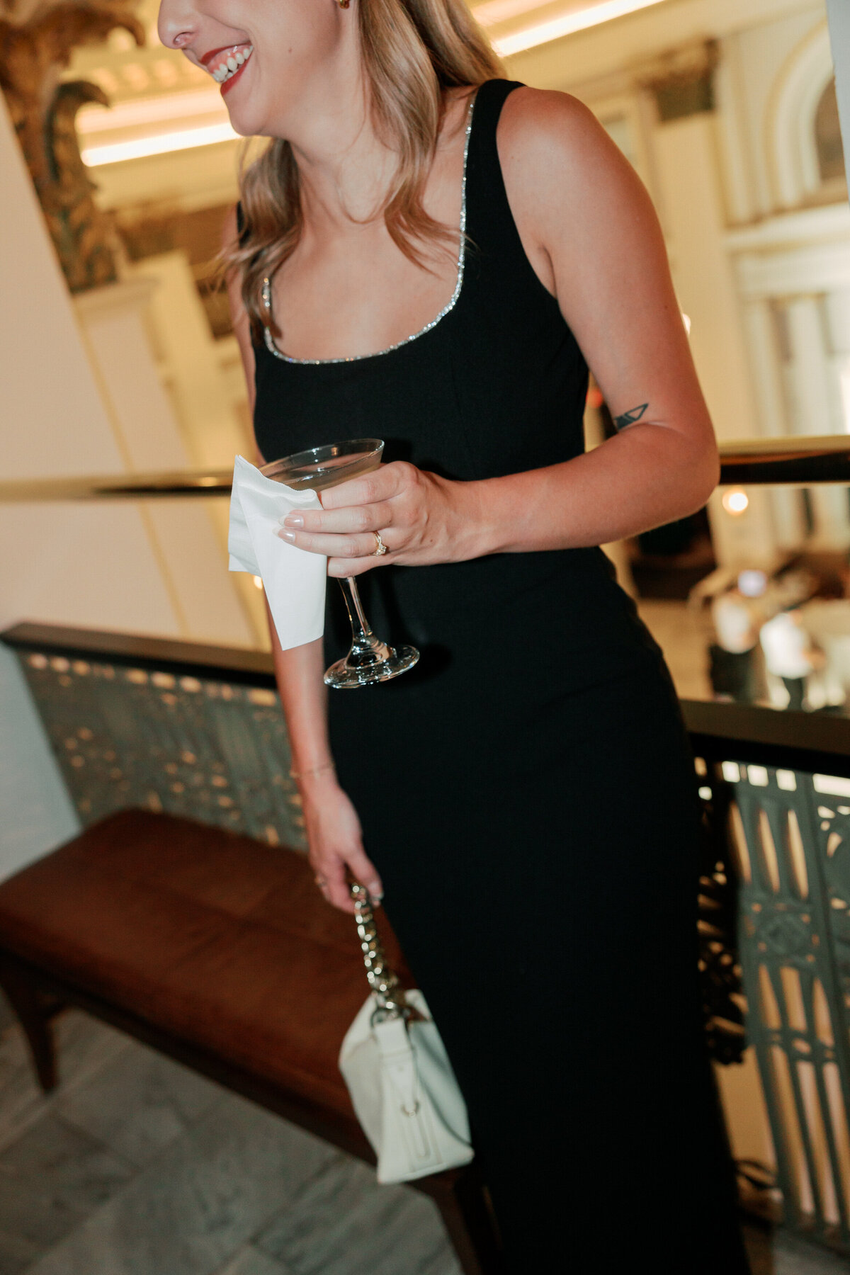 Wedding guest with martini and clutch in elegant black dress, shot by Philadelphia wedding photographer.