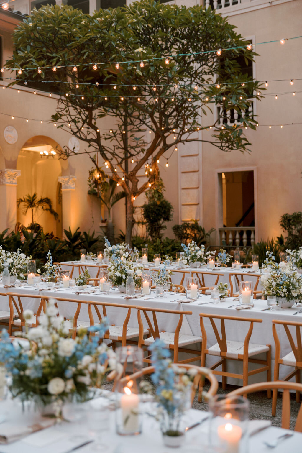 Dusky lighting with reception tables having blue and white florals on top in a courtyard