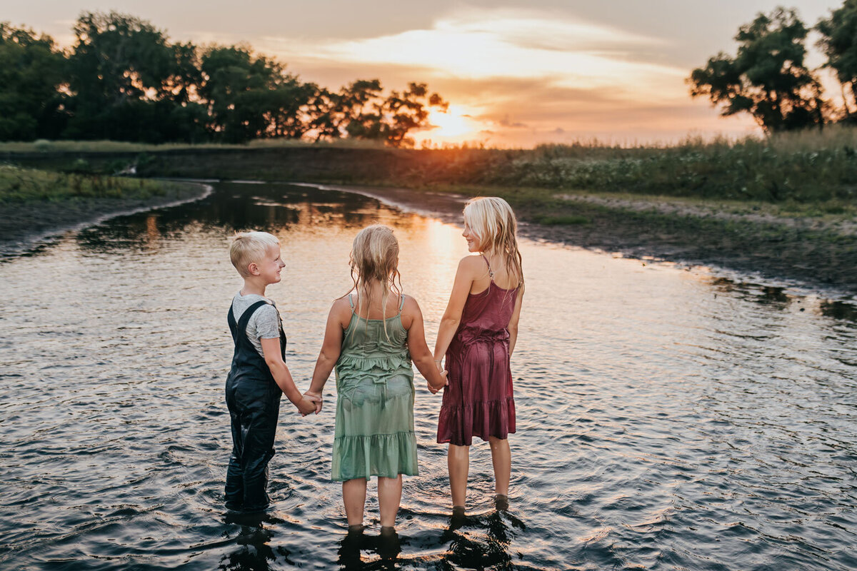siblinbs-holding-hands-at-sunset-in-creek