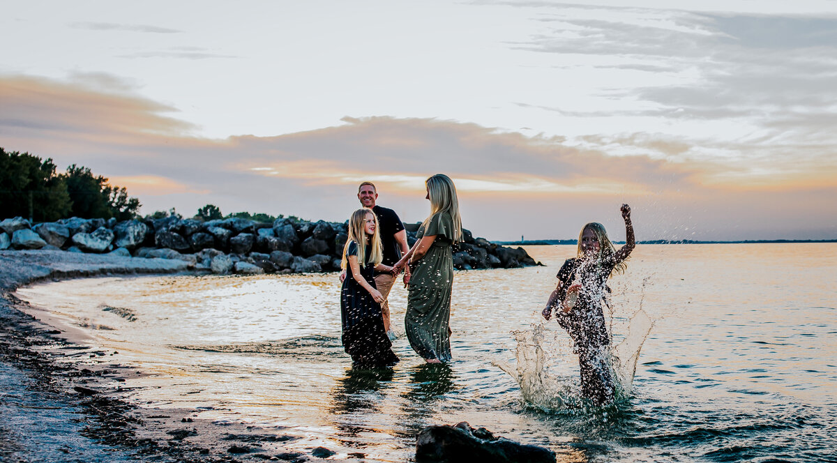 mom and daughter dancing together, dad is in background, younger daughter is kicking the water, they are all playing in lake Erie , toledo Maumee bay