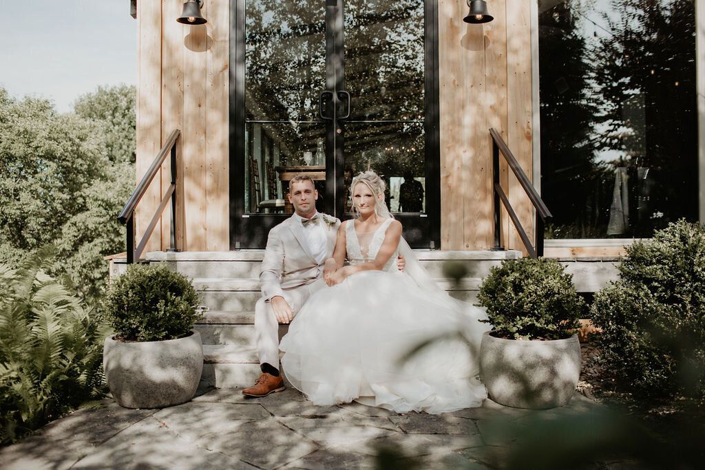 bride in a white gown and groom in a tan suit sitting on the limestone stairs of the Willowbrook wedding venue in the outdoor garden setting