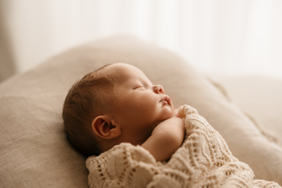 Photo of a newborn baby wrapped in a knitted blanket and lying on a pillow sleeping during a newborn photoshoot