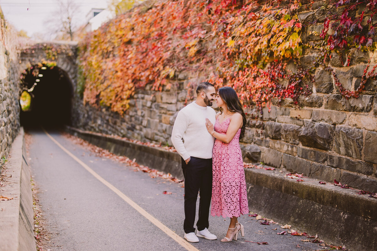 A couple sharing a moment in front of a colorful fall leaf wall by the wilkes street tunnel in old town alexandria md