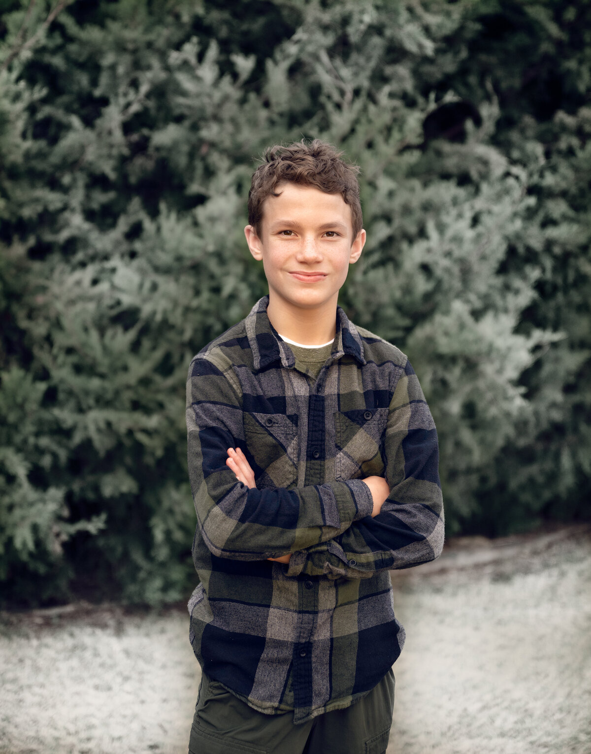 Outdoor family photo session in McKinney, TX on a frosty morning. The boy in the image is dressed in dark greens, flannel, and standing in front of cedar trees.