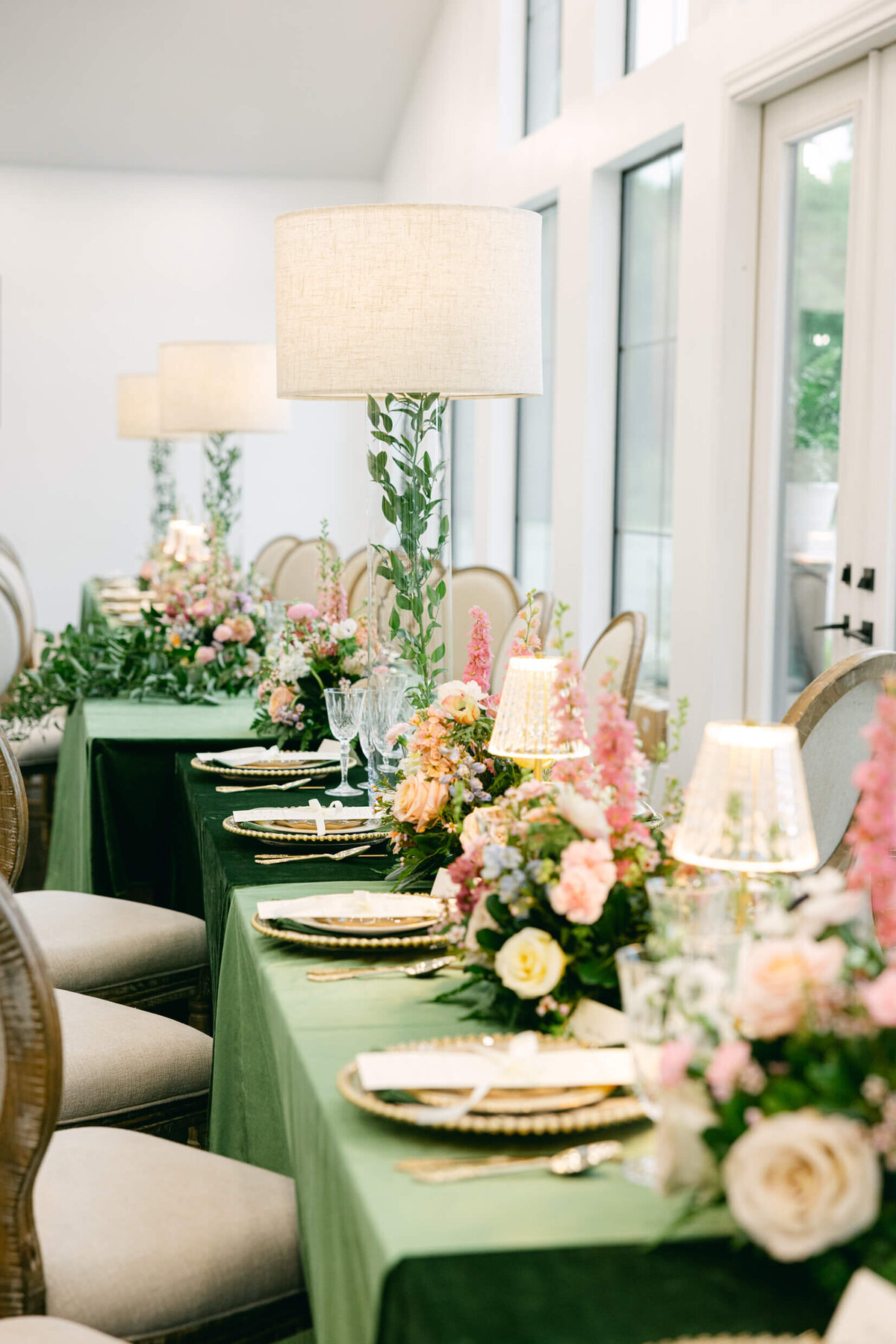 A wedding day photo of the tables in the reception hall that are covered in green linens with florals & candles on top