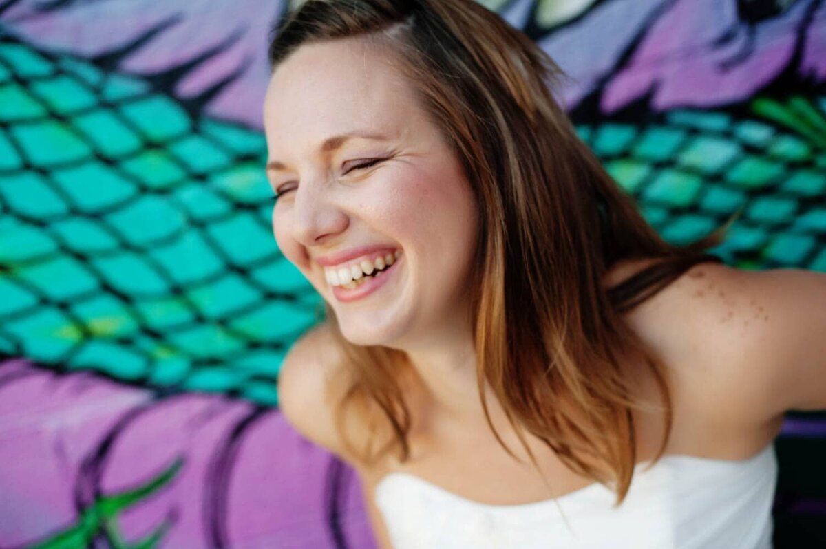 a bride laughs happily in front of a colorful purple and teal wall