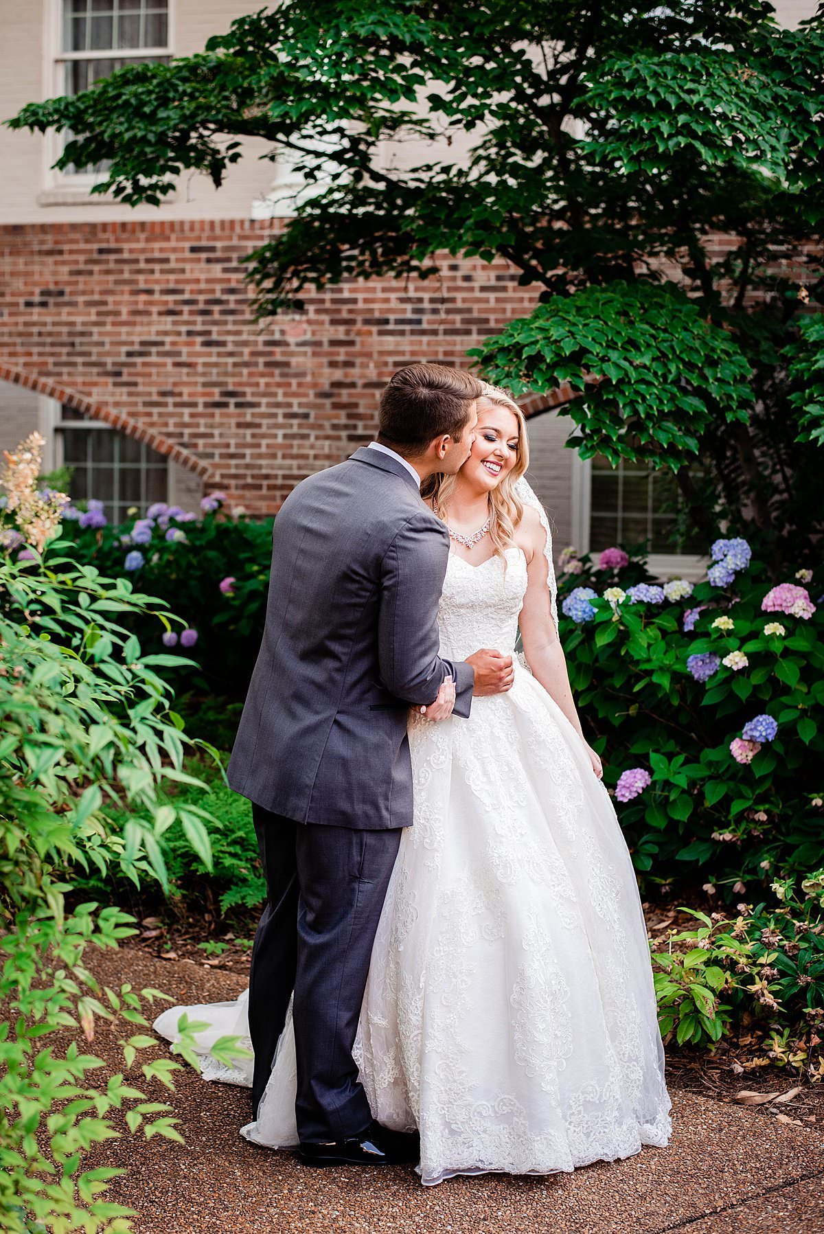 Couple standing together in outdoor courtyard with natural plants and hydrangeas around them