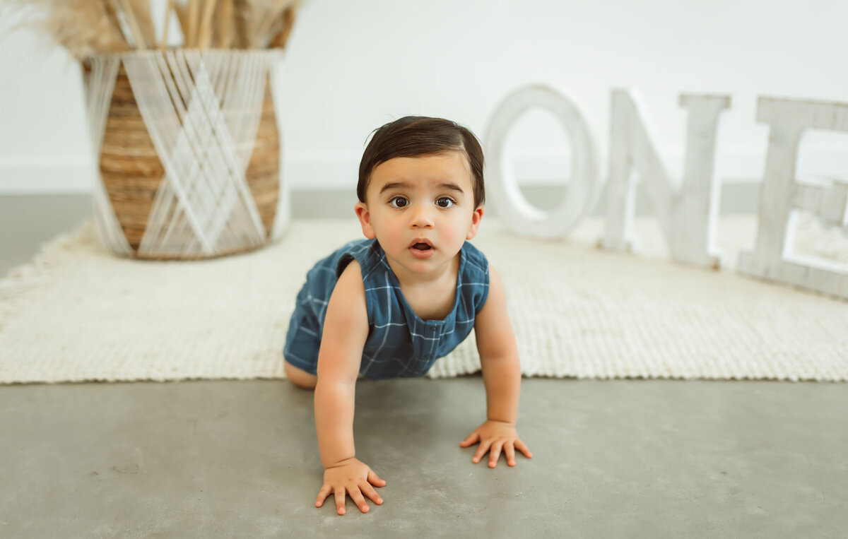 boy crawling on a concrete floor looking straight up front. He is celebrating turning one year old