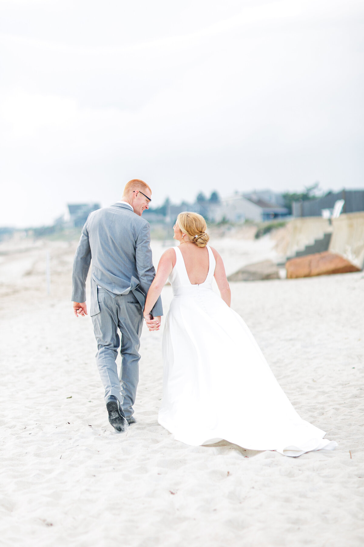 A bride and groom holding hands and walking away from the camera representing a Cape Cod beach wedding