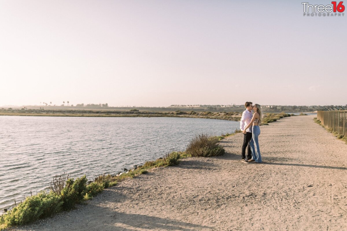 Engaged couple stop on a trail at the Bolsa Chica Ecological Reserve to share a kiss