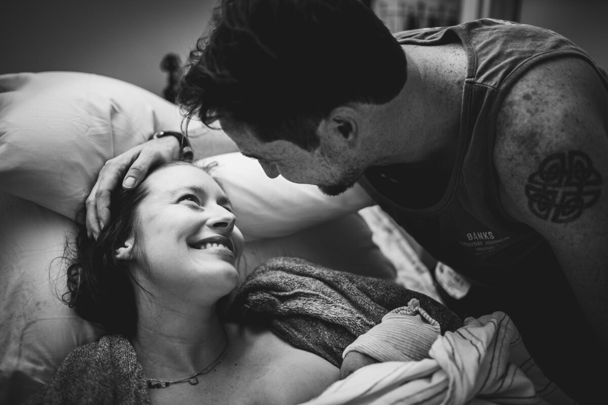woman gazes at her husband lovingly as she breastfeeds their baby