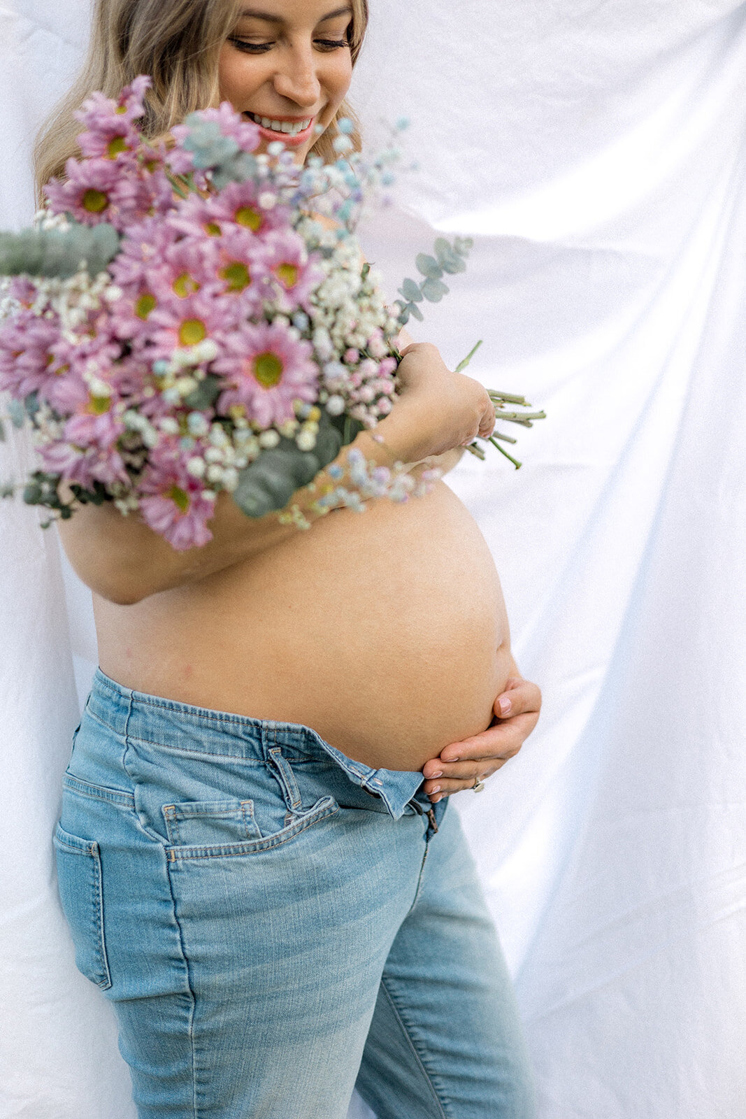 A pregnant woman holds her belly while holding flowers