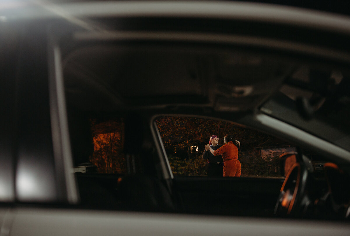 An artistic view through a car window focusing on two people dressed in orange, embracing in a warmly lit night setting