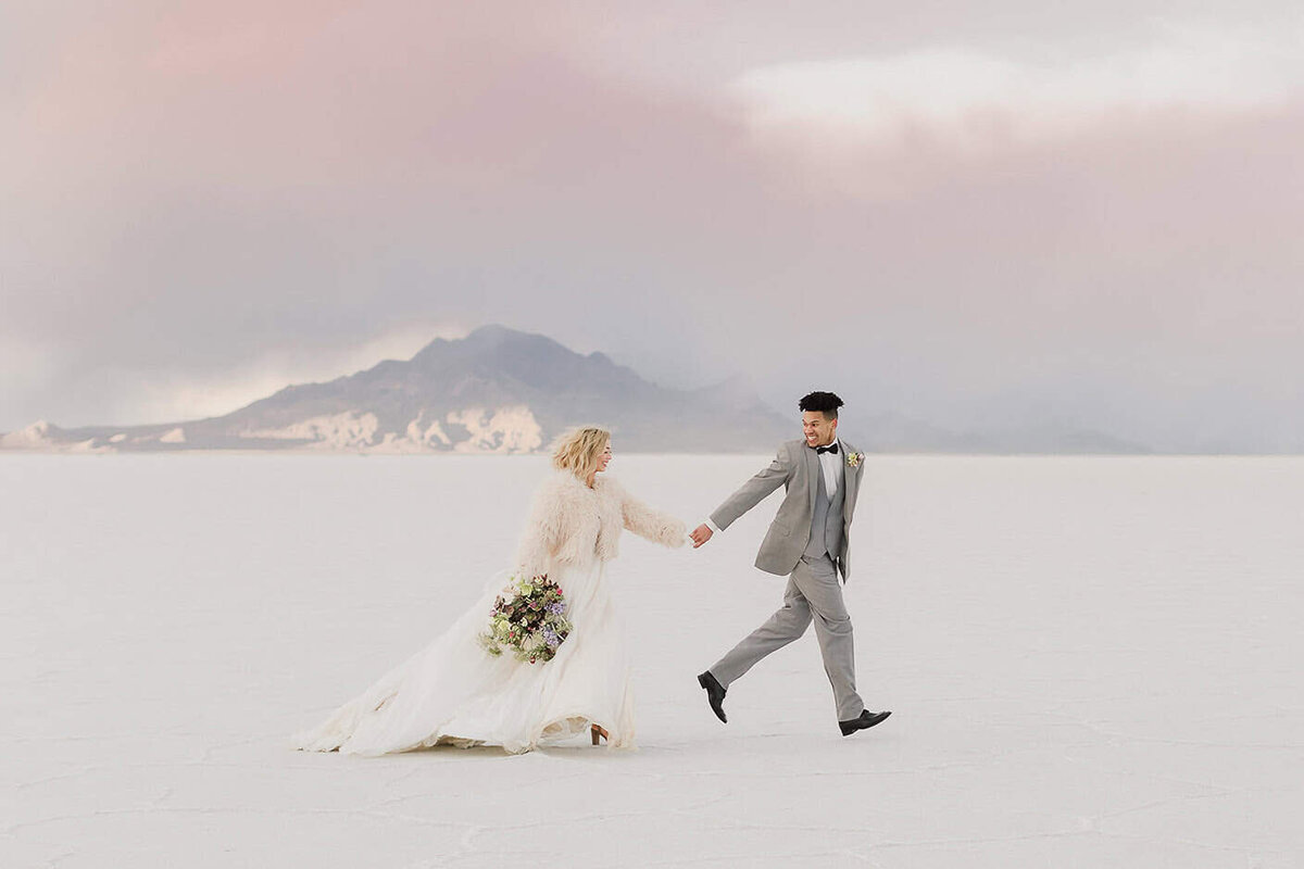 A bride and groom run across the beautiful landscape of the salt flats near Utah at sunset.