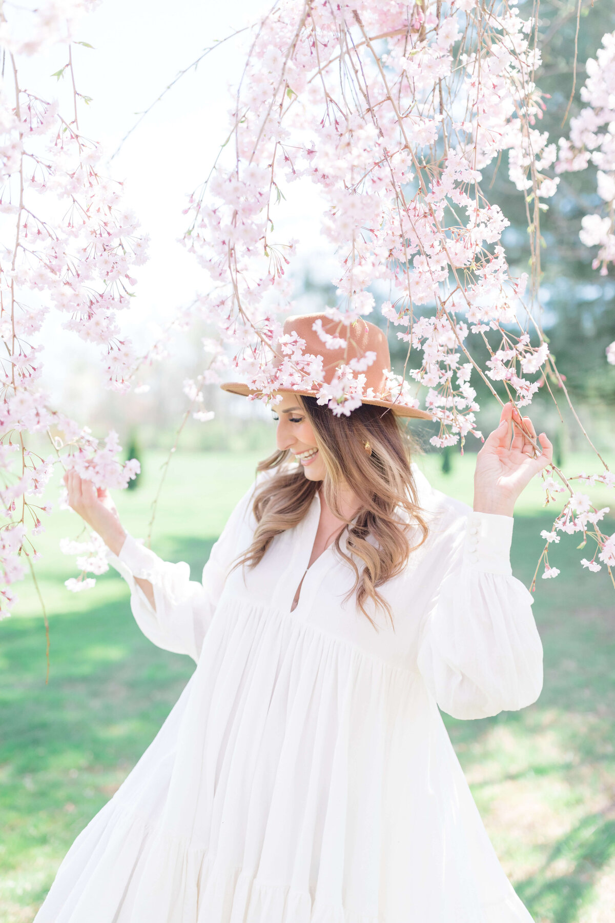 woman in white dress and brown hat outside with cherry blossom