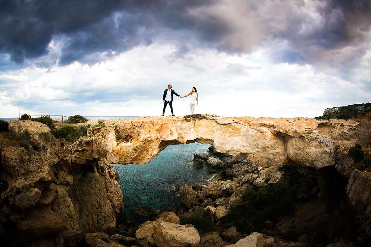 Bride & Groom hold hands on a bridge over the sea under a moody sky