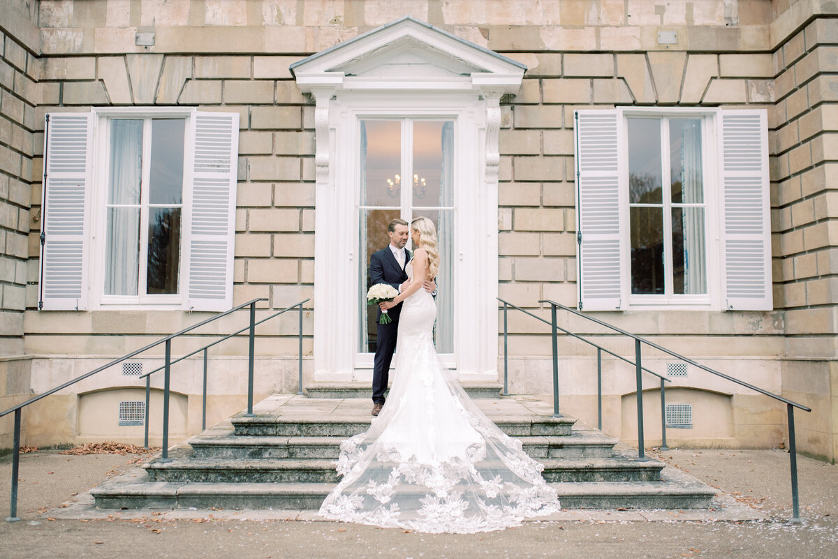 Bride and groom stood on the steps at York house cuddled together, the brides dress is fanned down the steps as they embrace. The image is edited in a light and airy style