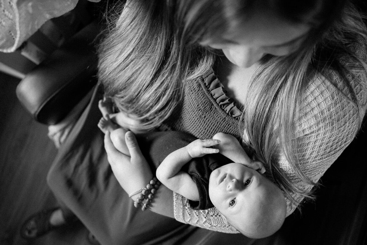 Photo looking down on infant who is in their mothers arms staring back up at the camera lens.