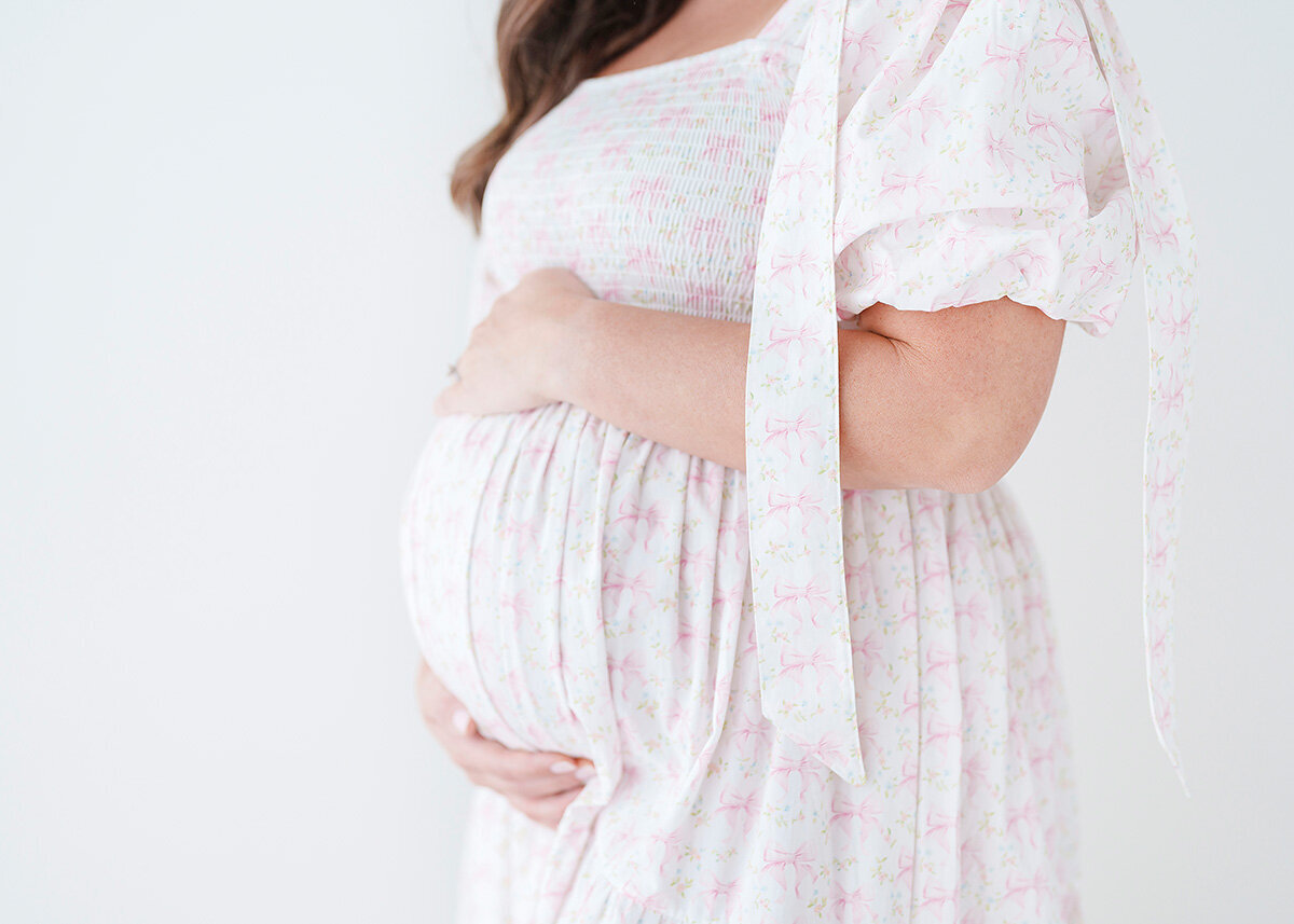 maternity client photoraphed in st simon island studio with a white and pink bow dress