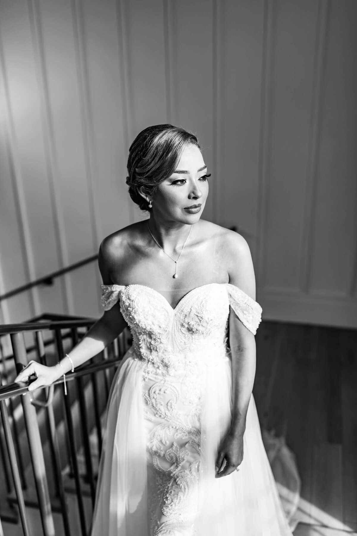 black and white image of a bride standing in on staircase, in front of large window