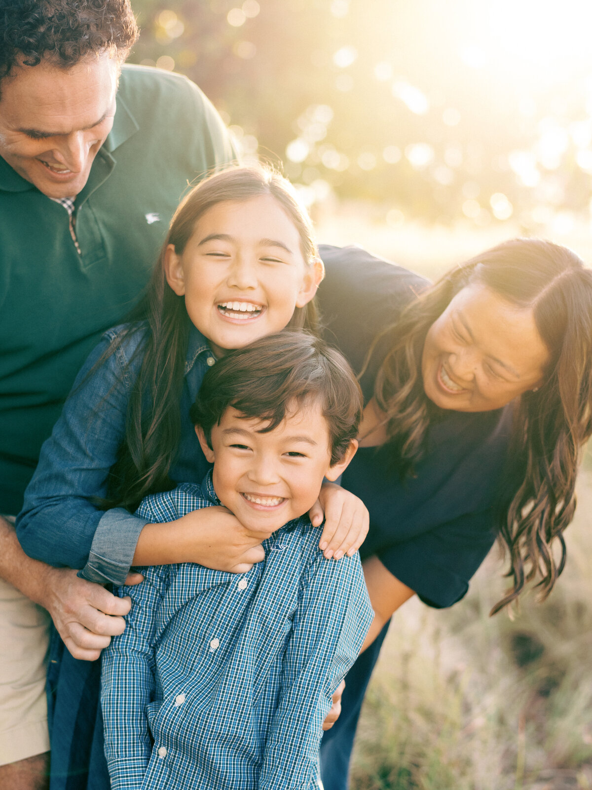 family of four tickling each other while backlit by sun during a fall mini session at the NC Museum of Art.  Image by Raleigh family photographer A.J. Dunlap Photography.
