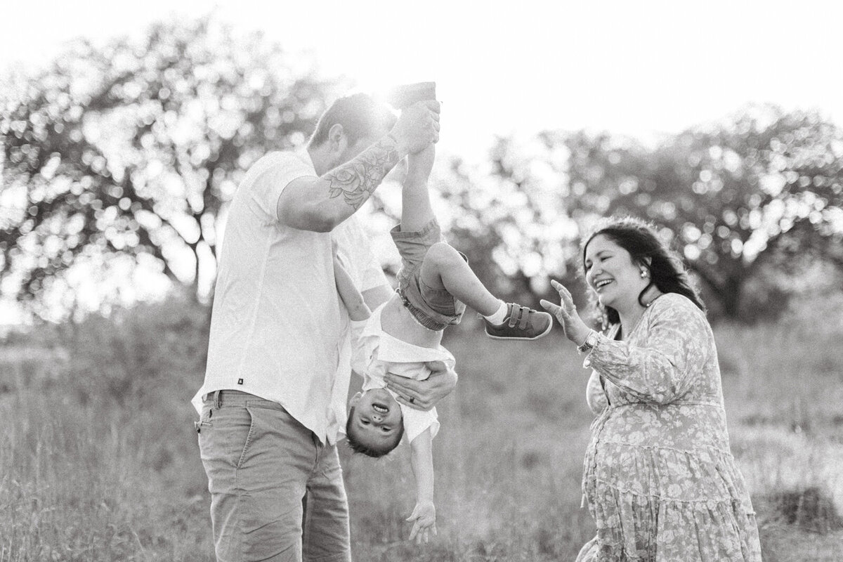 Black and white maternity photo of a pregnant woman with her family in a field, photographed by San Antonio family photographer Sara James.